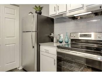 A black refrigerator stands next to a stainless steel oven in a kitchen.